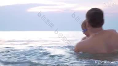 年轻的爸爸和儿子戴着护目镜在海里洗澡，爸爸旋转着孩子，然后在他摔倒的时候抱着他